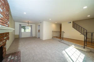 living room with beige carpet, brick fireplace, and large window with curtains.