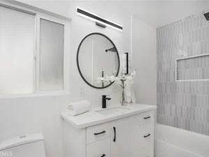 bathroom with white walls, round mirror, black fixtures, and gray tile shower