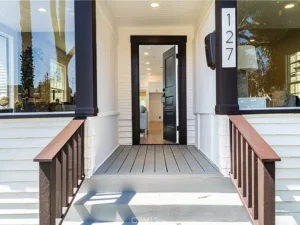 Front porch of a house with a white exterior and brown accents with an open door.