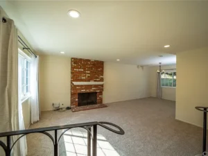 living room with beige carpet, featuring a red brick fireplace centered on a cream wall.