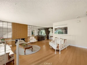 living room with a brick fireplace, mirrored wall, wooden floors, floral armchairs, and a glass coffee table