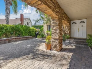 A stone archway frames a paved patio leading to double white doors.