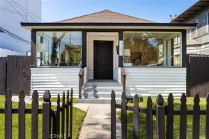 single-story real estate house with a white facade and dark trim, and a wooden fence