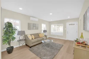 living room with beige walls, gray sofa with yellow pillows faces a glass coffee table