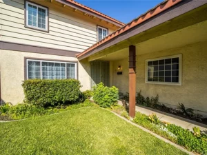 real estate house entrance with a neatly manicured lawn, garden shrubs, and a covered porch.